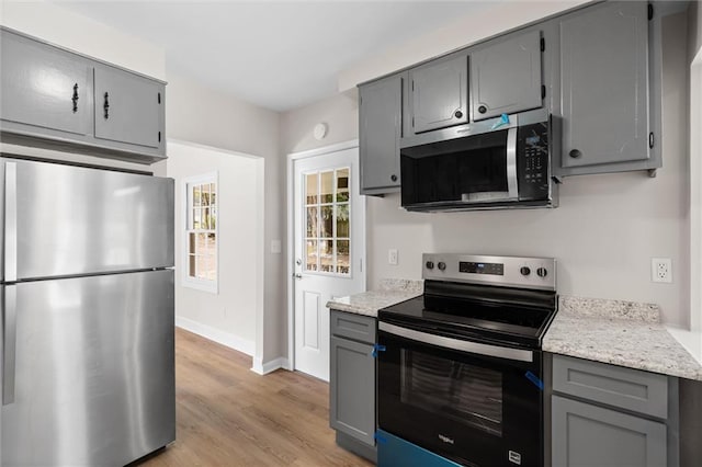 kitchen featuring gray cabinetry, baseboards, light wood-style floors, appliances with stainless steel finishes, and light stone countertops