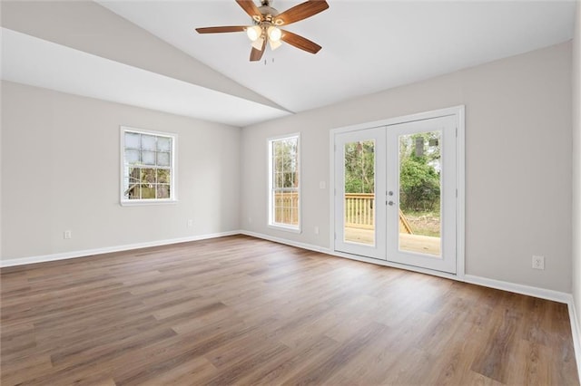 empty room featuring a wealth of natural light, vaulted ceiling, baseboards, and wood finished floors