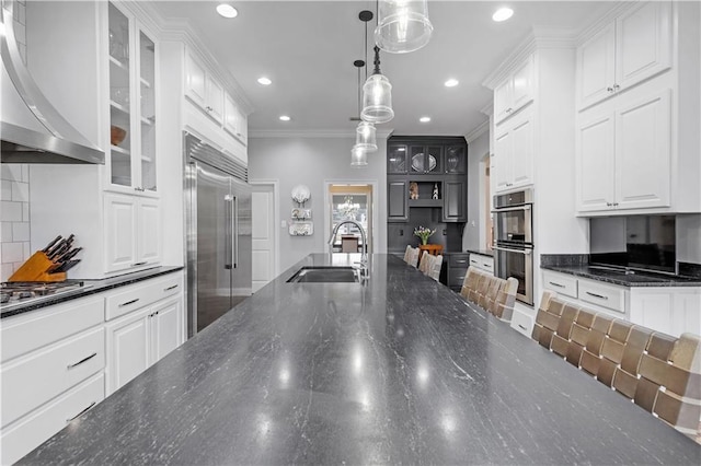 kitchen featuring pendant lighting, sink, white cabinets, stainless steel appliances, and wall chimney range hood