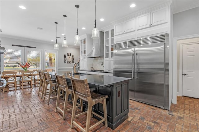 kitchen featuring ornamental molding, stainless steel built in refrigerator, a kitchen island with sink, and white cabinets