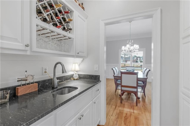 kitchen with sink, white cabinets, hanging light fixtures, crown molding, and light wood-type flooring