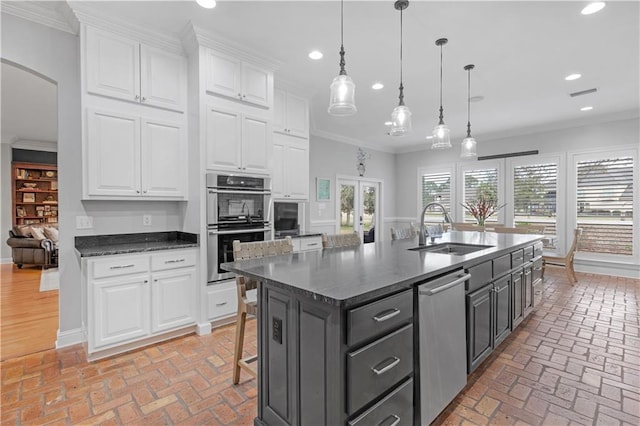 kitchen with pendant lighting, sink, white cabinetry, ornamental molding, and an island with sink