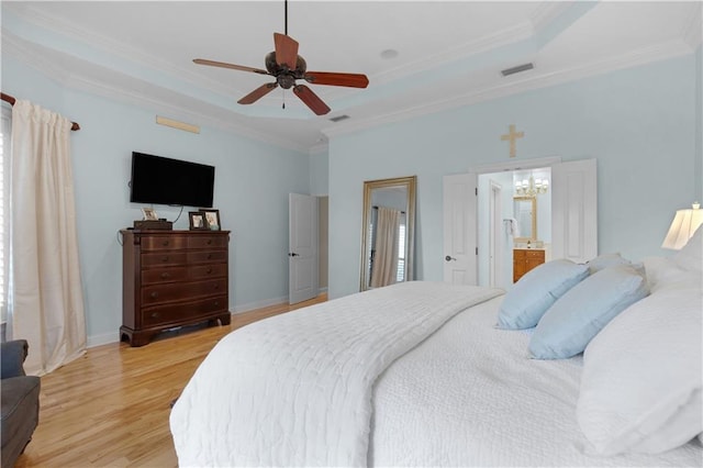 bedroom featuring crown molding, connected bathroom, a tray ceiling, and light wood-type flooring