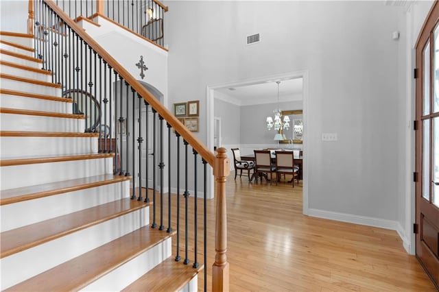 entrance foyer with crown molding, a towering ceiling, a chandelier, and light wood-type flooring