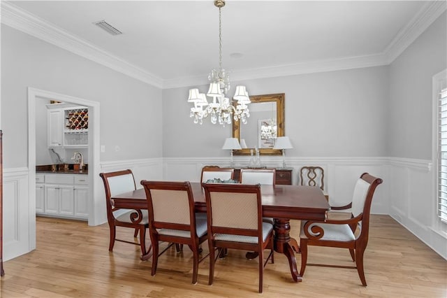 dining space featuring ornamental molding, sink, light hardwood / wood-style floors, and a notable chandelier