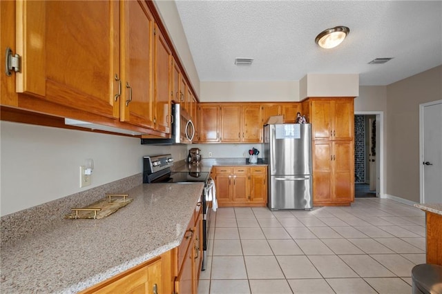 kitchen featuring a textured ceiling, stainless steel appliances, light stone counters, and light tile patterned floors