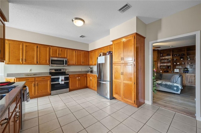 kitchen featuring light tile patterned flooring, a textured ceiling, and appliances with stainless steel finishes