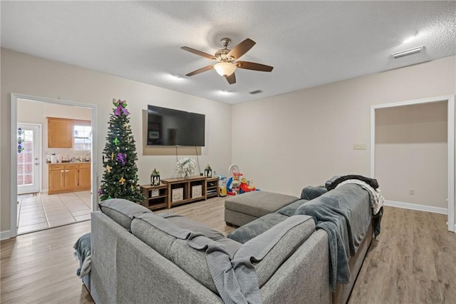 living room with a textured ceiling, ceiling fan, and light hardwood / wood-style flooring