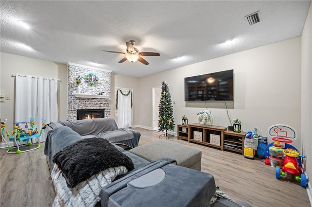 living room with ceiling fan, hardwood / wood-style floors, a textured ceiling, and a fireplace