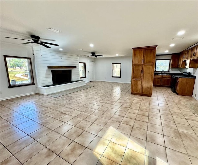 unfurnished living room featuring ceiling fan, a large fireplace, light tile patterned floors, and sink