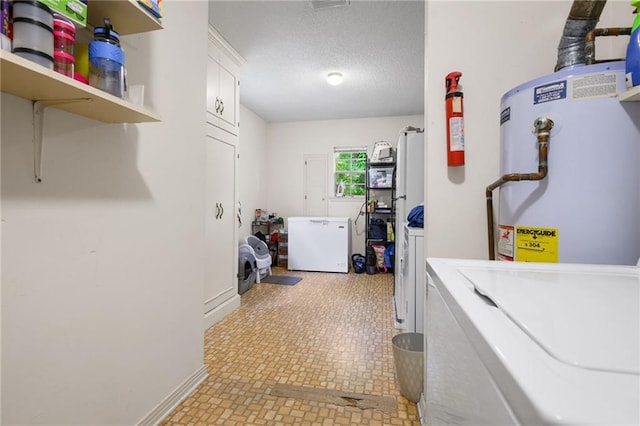 washroom with washer and dryer, baseboards, a textured ceiling, cabinet space, and water heater