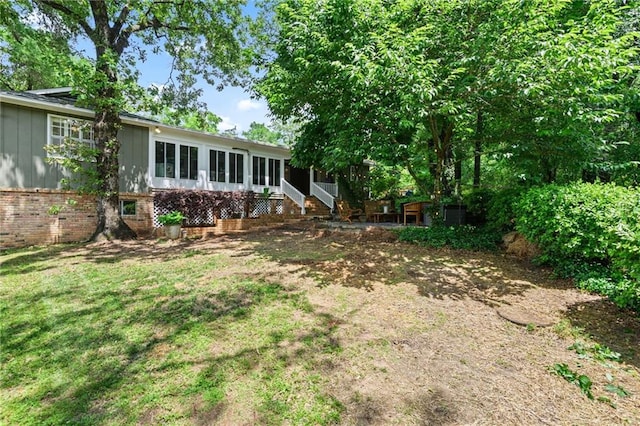 exterior space featuring brick siding, board and batten siding, a yard, and a sunroom