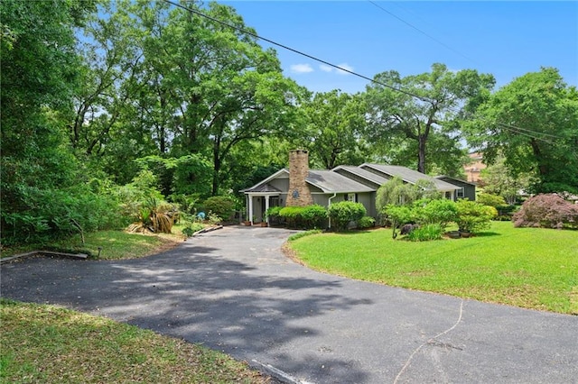view of front facade featuring a chimney, aphalt driveway, and a front yard