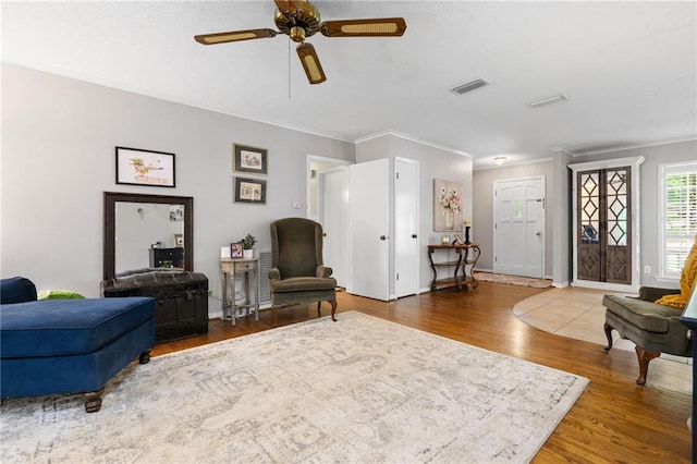 living room featuring crown molding, a ceiling fan, baseboards, wood finished floors, and visible vents