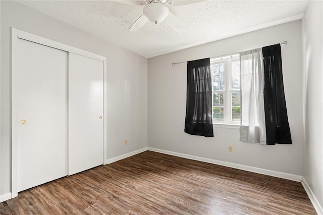 unfurnished bedroom with a textured ceiling, ceiling fan, wood finished floors, baseboards, and a closet