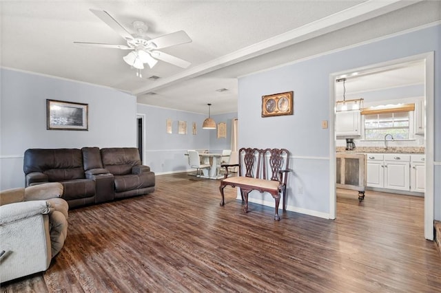 living area featuring dark wood-type flooring, ornamental molding, baseboards, and a ceiling fan