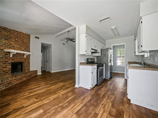 kitchen featuring dark hardwood / wood-style floors, a fireplace, appliances with stainless steel finishes, white cabinetry, and lofted ceiling