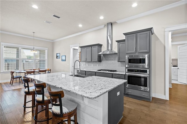 kitchen featuring appliances with stainless steel finishes, a kitchen island with sink, wall chimney range hood, washer / clothes dryer, and sink