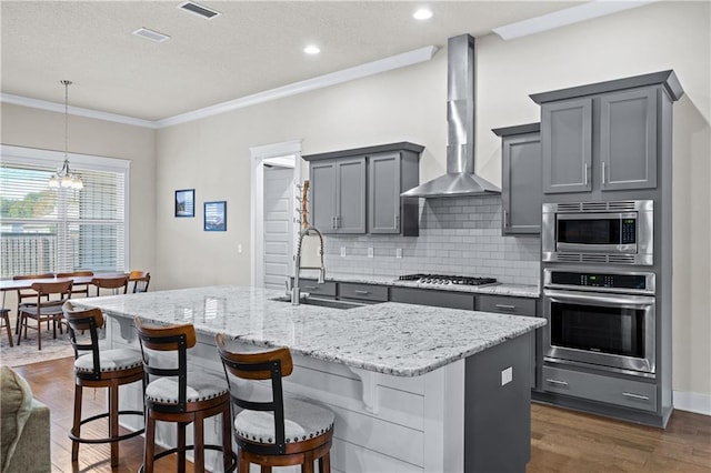 kitchen featuring wall chimney range hood, sink, a kitchen island with sink, gray cabinetry, and stainless steel appliances