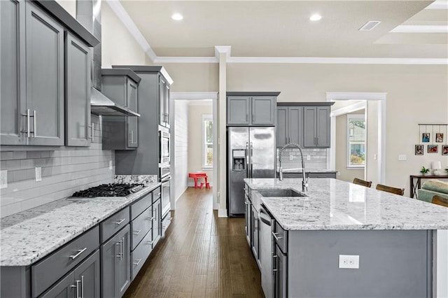 kitchen featuring backsplash, gray cabinets, crown molding, appliances with stainless steel finishes, and an island with sink