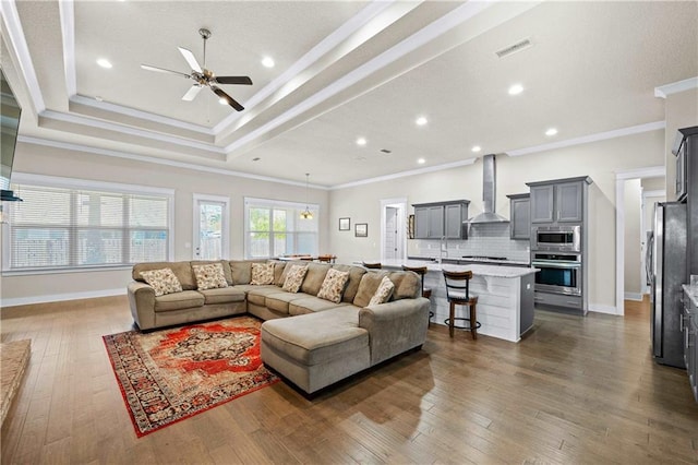 living room with ceiling fan, dark hardwood / wood-style flooring, crown molding, and a tray ceiling