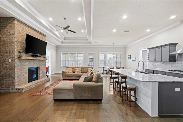 living room featuring ceiling fan, dark hardwood / wood-style floors, a fireplace, ornamental molding, and sink