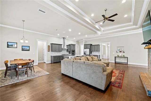 living room with dark wood-type flooring, ceiling fan with notable chandelier, a tray ceiling, and ornamental molding