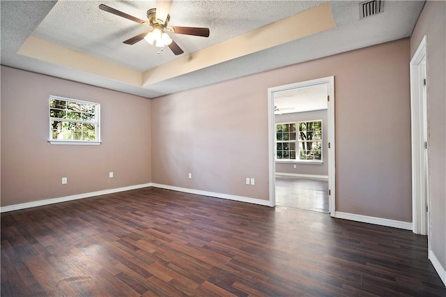 empty room with a tray ceiling, dark hardwood / wood-style flooring, a healthy amount of sunlight, and a textured ceiling