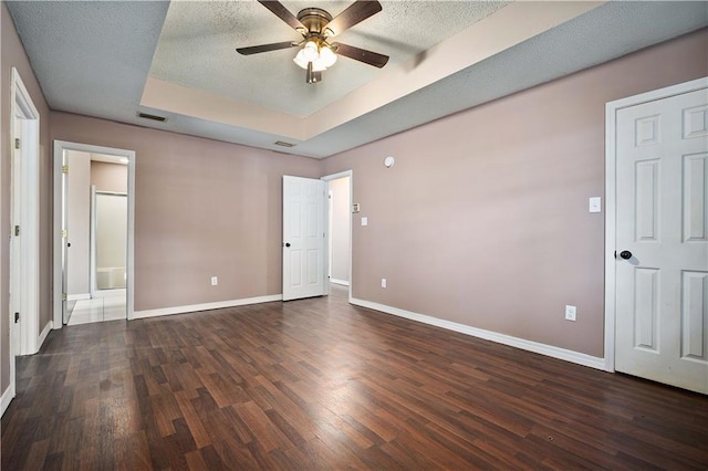 unfurnished bedroom featuring a textured ceiling, dark hardwood / wood-style flooring, a tray ceiling, and ceiling fan