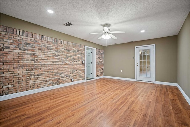 spare room featuring ceiling fan, light wood-type flooring, a textured ceiling, and brick wall