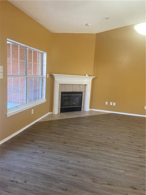 unfurnished living room featuring wood-type flooring and a tiled fireplace