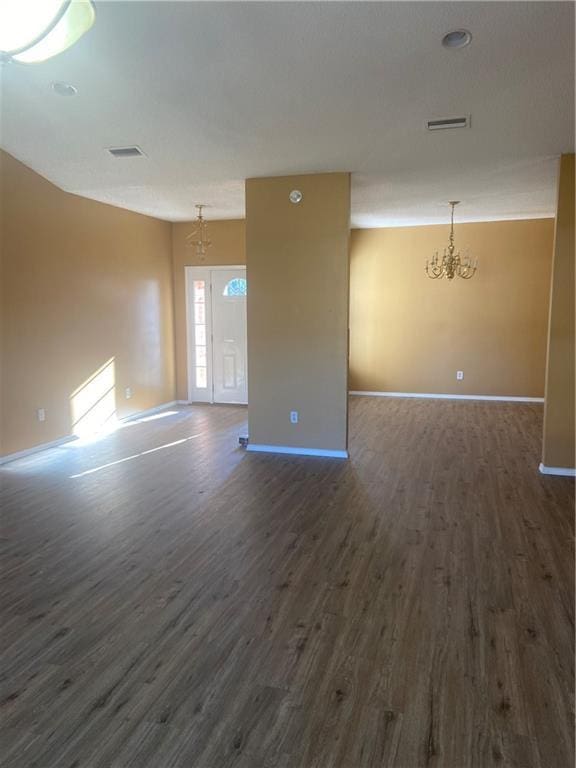 empty room with dark hardwood / wood-style flooring and a notable chandelier