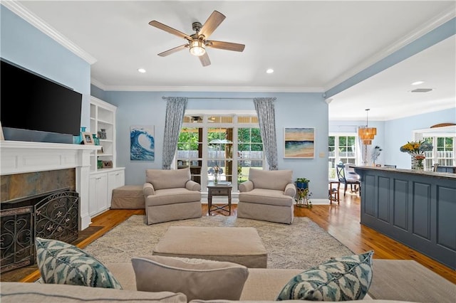 living room featuring a fireplace with flush hearth, wood finished floors, ceiling fan with notable chandelier, ornamental molding, and recessed lighting