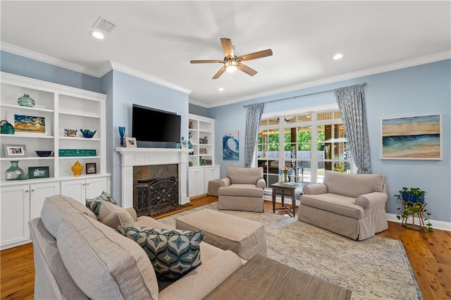 living area featuring ceiling fan, visible vents, a fireplace with flush hearth, wood finished floors, and ornamental molding