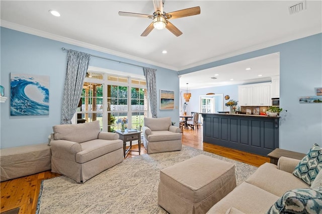 living area featuring ceiling fan, light wood-style flooring, recessed lighting, visible vents, and ornamental molding