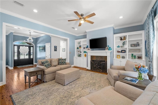 living area featuring a ceiling fan, visible vents, a tiled fireplace, baseboards, and wood-type flooring