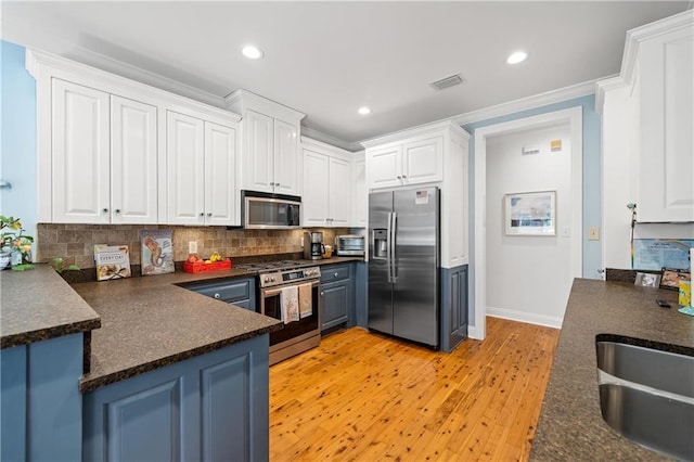 kitchen featuring white cabinets, stainless steel appliances, dark countertops, and visible vents