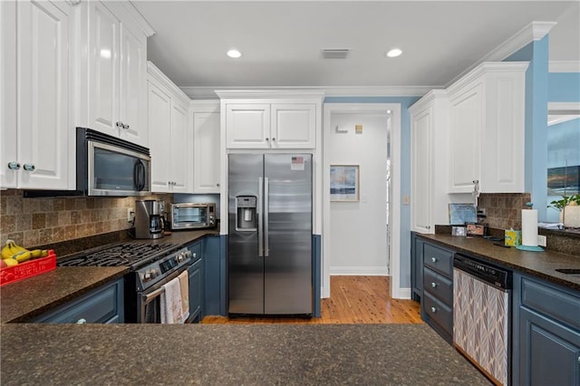 kitchen featuring white cabinets, crown molding, dark countertops, appliances with stainless steel finishes, and light wood-type flooring