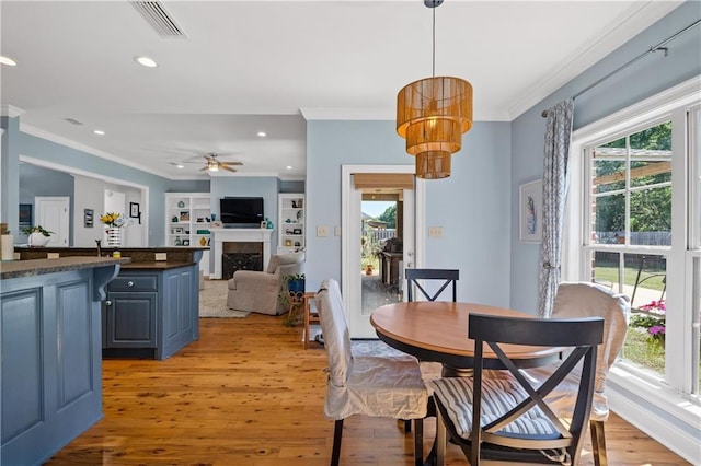 dining room with a high end fireplace, ornamental molding, ceiling fan with notable chandelier, and light wood-type flooring