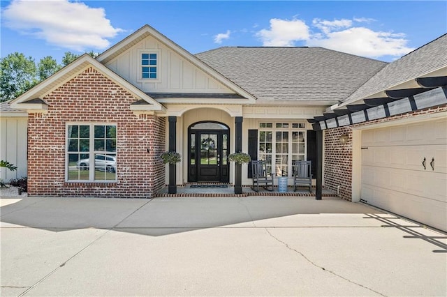 entrance to property featuring board and batten siding, brick siding, covered porch, and a garage