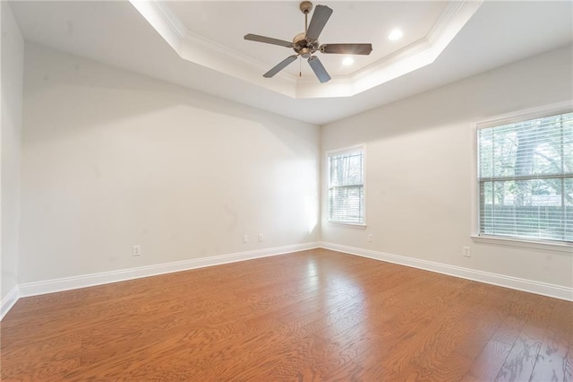 empty room featuring ornamental molding, a raised ceiling, baseboards, and wood finished floors