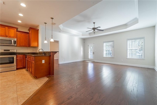 kitchen featuring a peninsula, a ceiling fan, appliances with stainless steel finishes, brown cabinets, and a tray ceiling