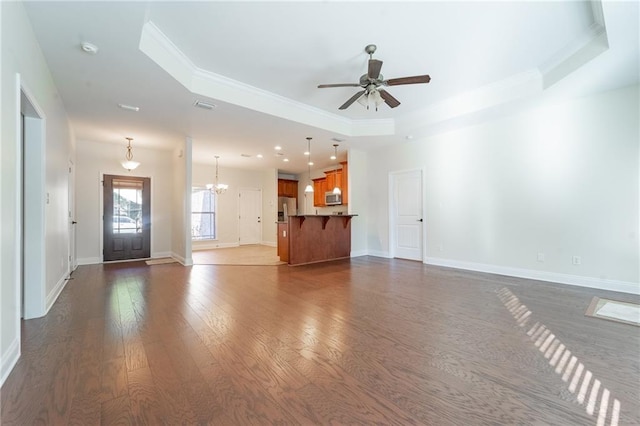 unfurnished living room with baseboards, a tray ceiling, dark wood-style flooring, and ceiling fan with notable chandelier