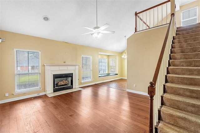 unfurnished living room featuring lofted ceiling, a fireplace with flush hearth, a ceiling fan, baseboards, and wood-type flooring