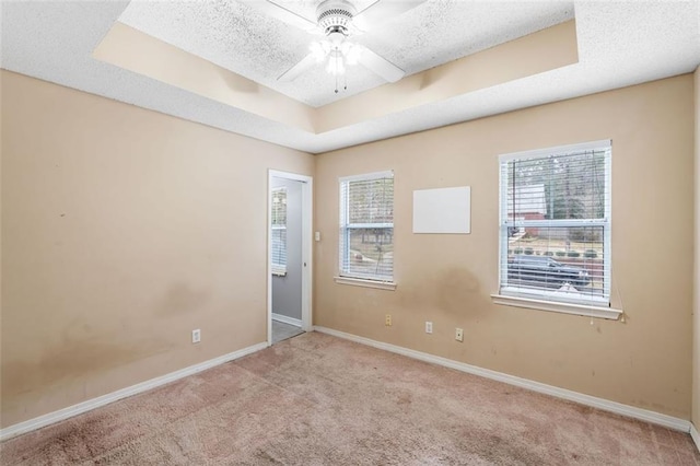 carpeted empty room featuring ceiling fan, baseboards, a raised ceiling, and a textured ceiling