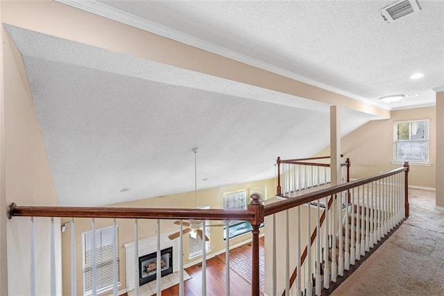 hallway featuring visible vents, wood finished floors, vaulted ceiling, a textured ceiling, and an upstairs landing