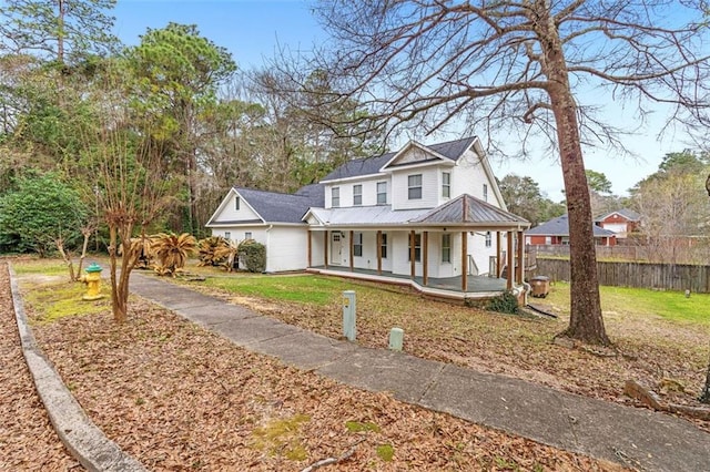 view of front of house featuring a porch, metal roof, a standing seam roof, fence, and a front lawn