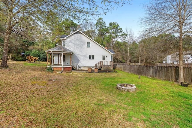 back of property featuring a fire pit, fence, and a lawn