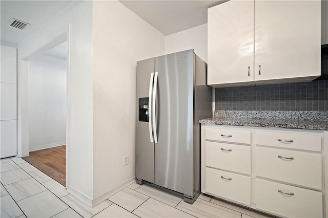 kitchen featuring visible vents, light stone counters, white cabinetry, stainless steel refrigerator with ice dispenser, and backsplash