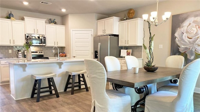 kitchen with appliances with stainless steel finishes, light hardwood / wood-style flooring, white cabinets, and tasteful backsplash